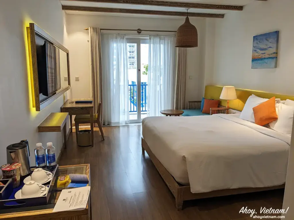 Inside my hotel room at the Risemount Premier Resort Da Nang, in Da Nang, Vietnam, showing a tv, bed, pillows, and balcony