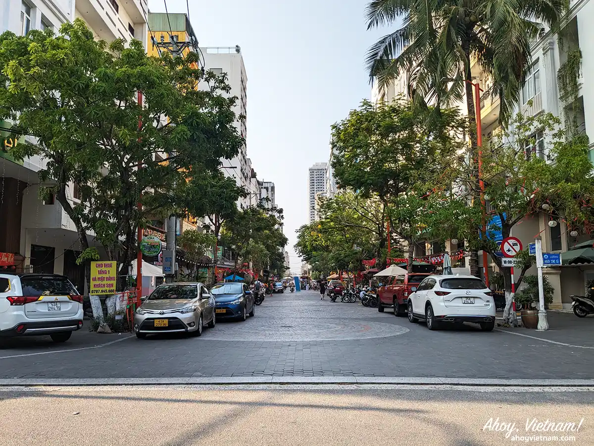 Tran Bach Dang Street, a cobblestone street lined with trees, shops, cars, hotels, tourists, and locals in Da Nang, Vietnam.