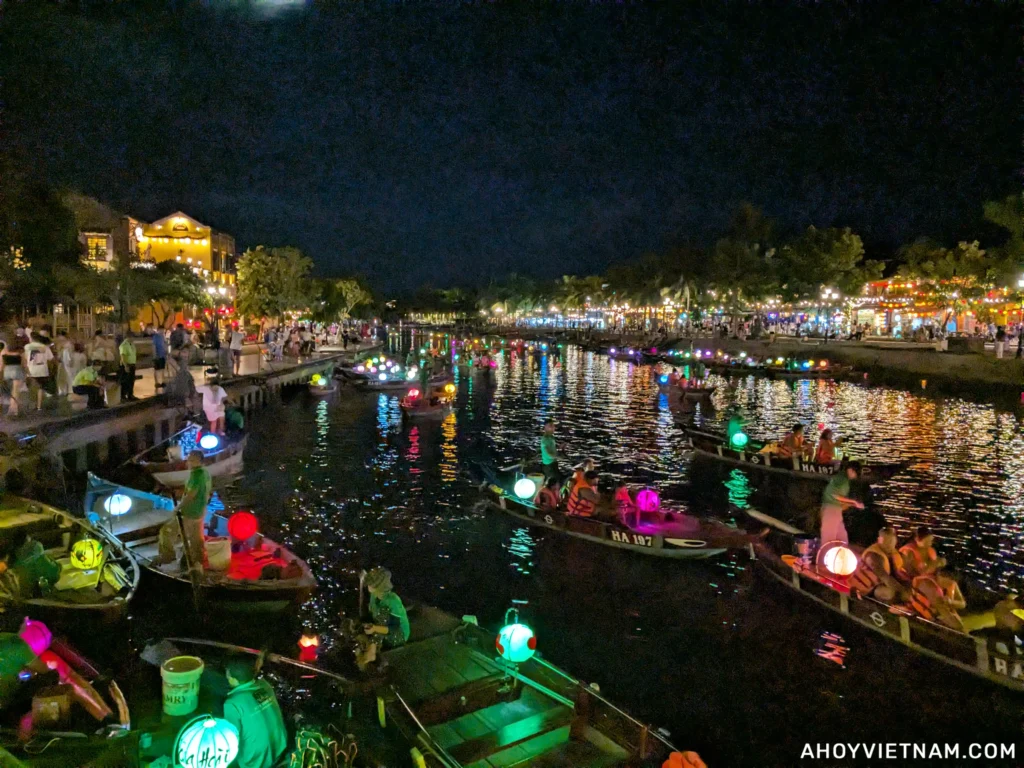Nighttime on the Thu Bon River in Hoi An Old Town, with tourists, boats, and lit lanterns.