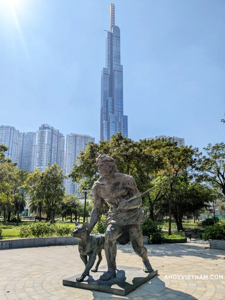 A statue of a hunter holding back a dog in front of the Landmark 81 skyscraper at Vinhomes Central Park.