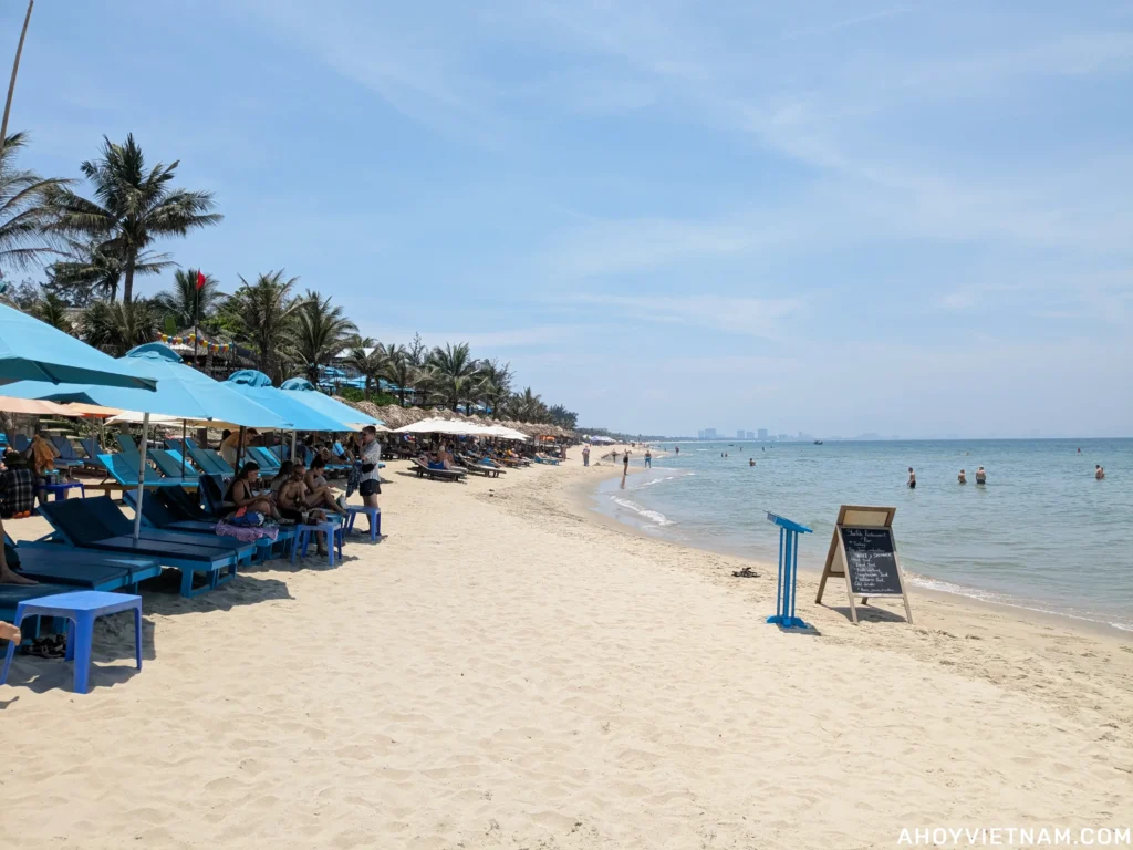 Tourists on sun loungers and swimming in the ocean at An Bang Beach in Hoi An, Vietnam.