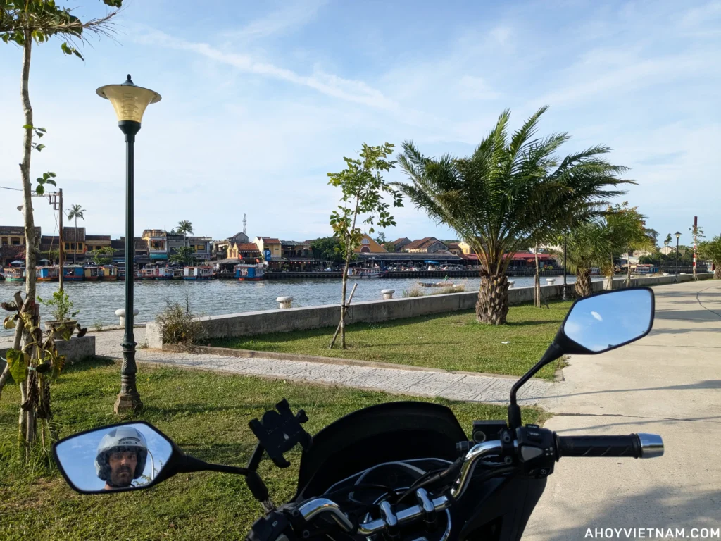View of Hoi An Old Town over the Thu Bon River, from the perspective of sitting on a scooter, with Anthony Giarratano's face visible in the side mirror.