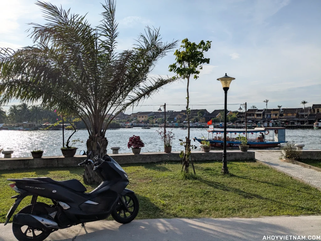 My black Honda PCX 150 scooter parked along the Thu Bon River in Hoi An.