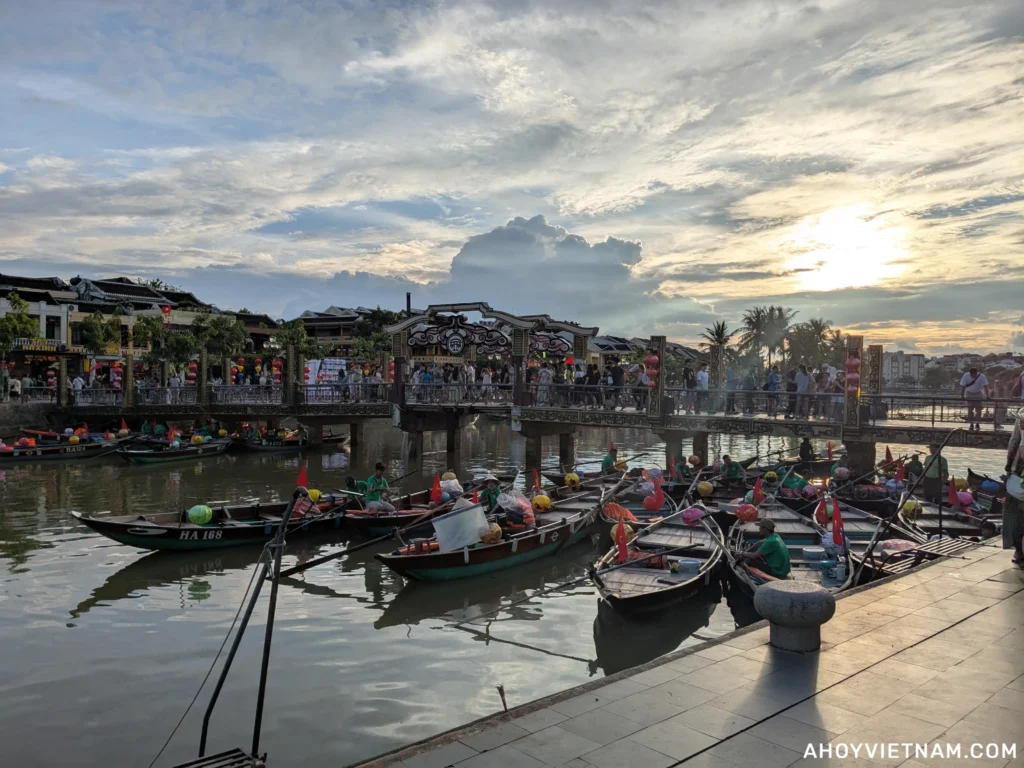The sun setting in Hoi An Old Town, with tourists crossing over the bridge to An Hoi Island and boats in the Thu Bon River