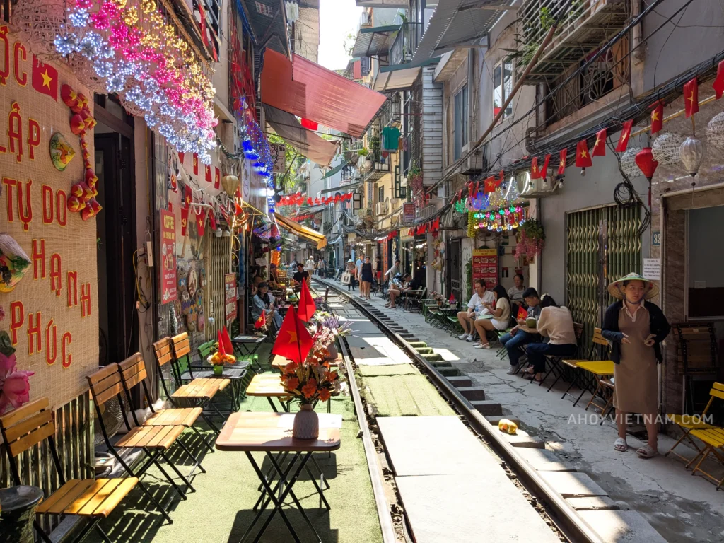 Looking down the tracks at Hanoi Train Street, with coffee shops, tables, locals, lights, and lanterns