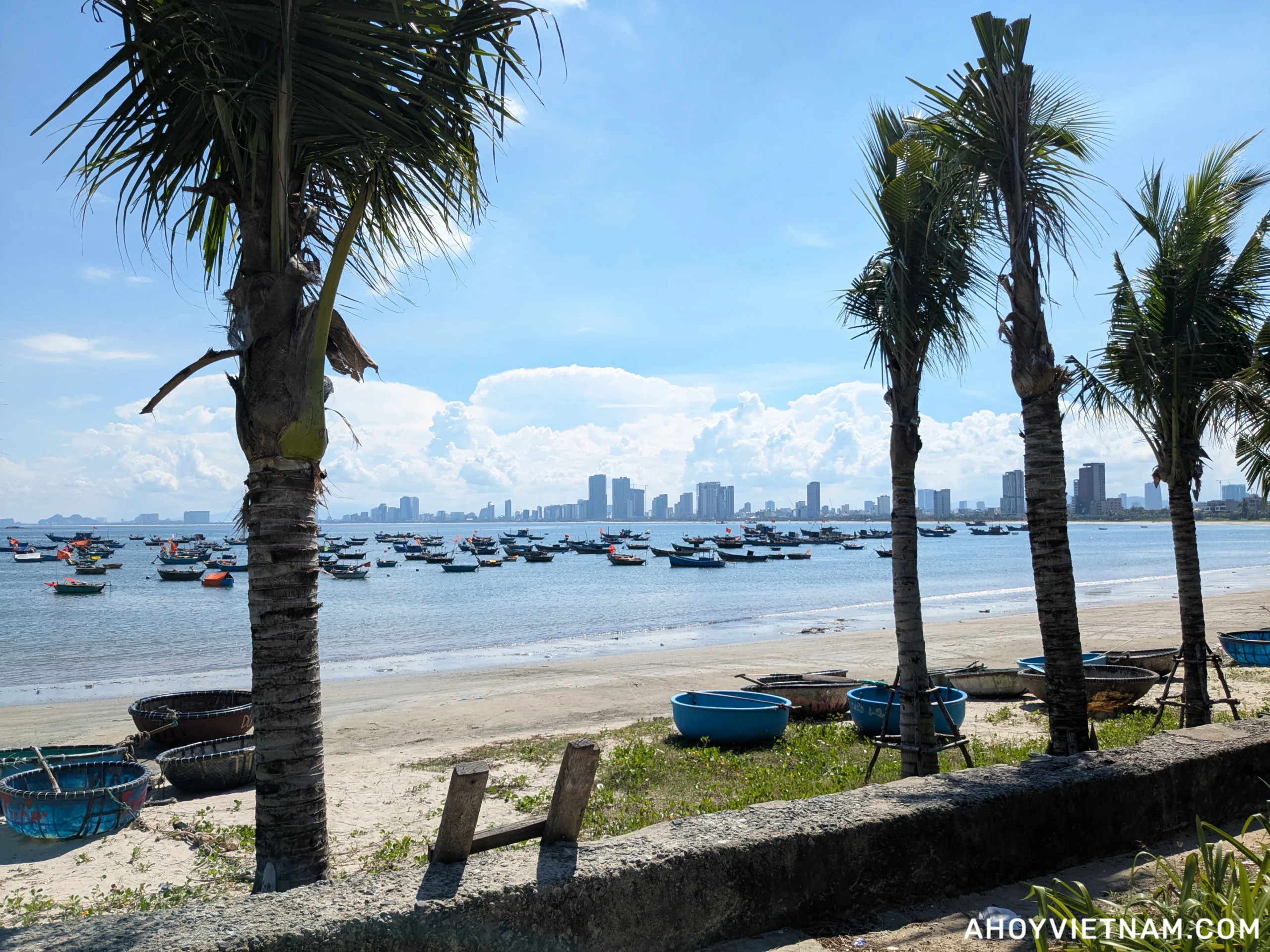 The coastline in Da Nang, Vietnam, with palm trees, fishing boats, and hotels in the distance