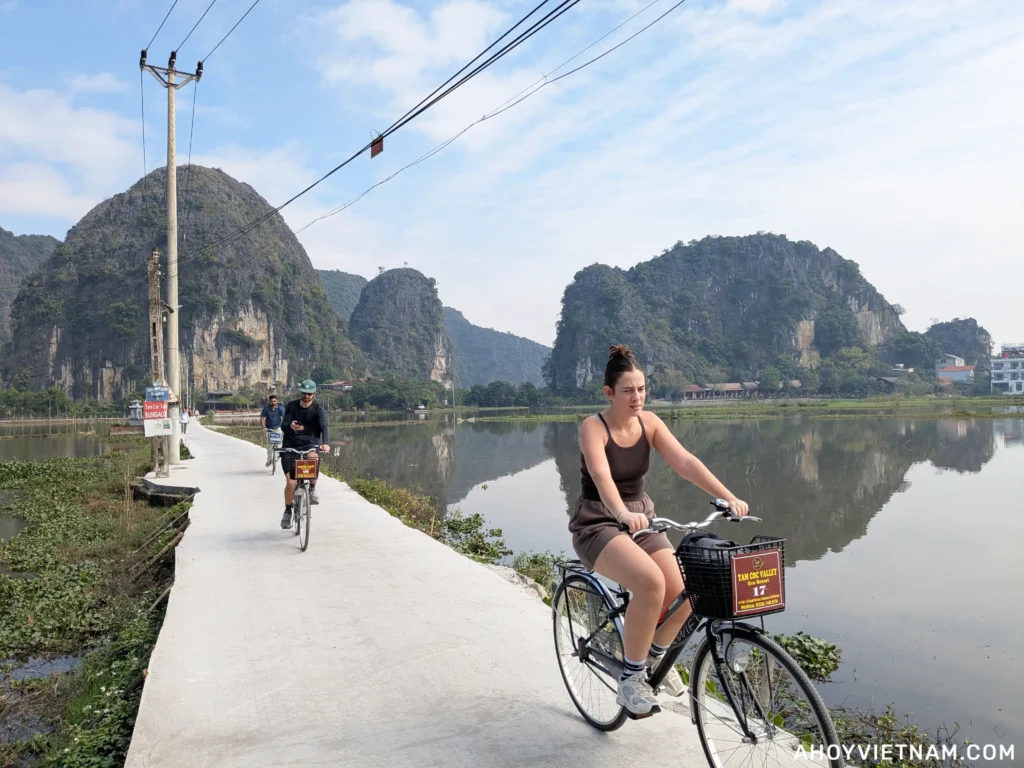 Travelers riding bikes on a small road over a lake in Ninh Binh, with limestone karsts in the distance
