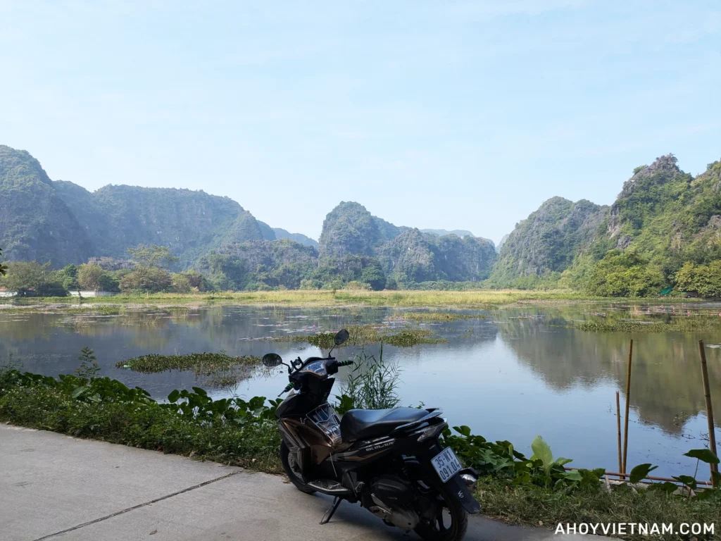 My rented Air Blade scooter parked in Ninh Binh with a lake and limestone karsts in the background